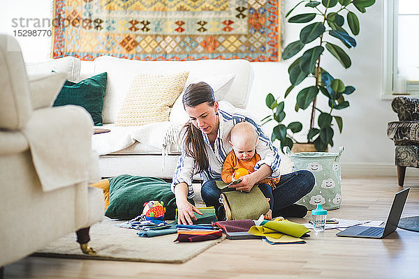 Multi-Tasking-Mutter mit Stoffmustern in voller Länge und Tochter  die zu Hause im Wohnzimmer arbeitet