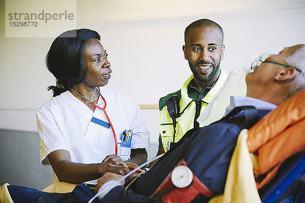Arzt im Gespräch mit Sanitäter während Behandlung eines reifen Geschäftsmannes auf Krankenhausbahre