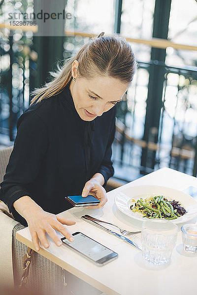 Selbstbewusste Geschäftsfrau benutzt ein Smartphone  während sie mit Kreditkarte in der Cafeteria im Büro sitzt