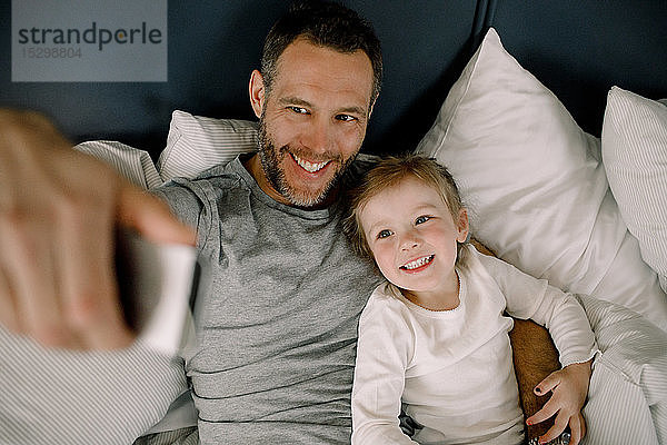 Schrägaufnahme eines glücklichen Vaters  der sich mit einer lächelnden Tochter auf dem Bett im Hotel eingenommen hat