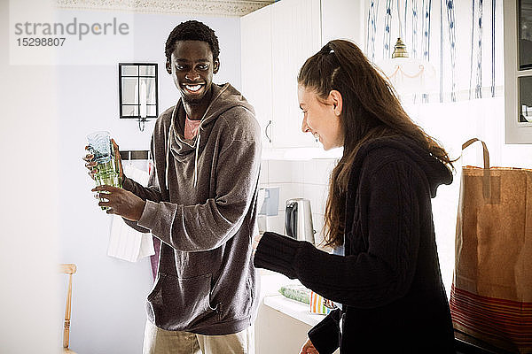 Junger Mann sieht lächelnde Freundin an  während er zu Hause in der Küche steht