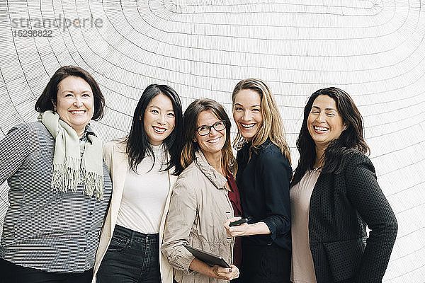 Porträt von lächelnden multiethnischen Geschäftsfrauen  die am Arbeitsplatz an der Wand stehen