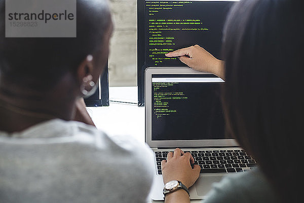 Rückansicht einer Unternehmerin  die auf Codes auf einem Computermonitor zeigt  an einen männlichen Hacker im Büro
