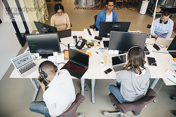 Schrägansicht von IT-Fachleuten  die im kreativen Büro am Schreibtisch sitzen