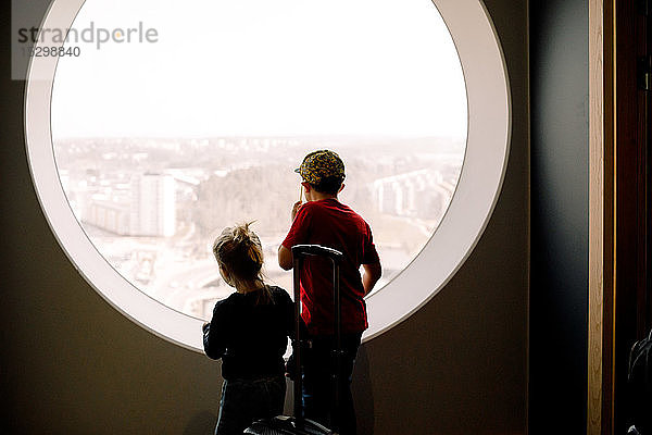 Geschwister schauen durch das Fenster  während sie im Hotelzimmer stehen