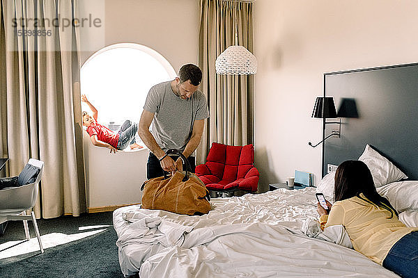 Mann packt Tasche  während Frau am Bett im Hotel telefoniert
