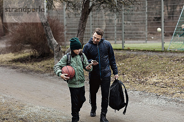 Vater und Sohn benutzen im Winter beim Gehen auf der Straße Mobiltelefone