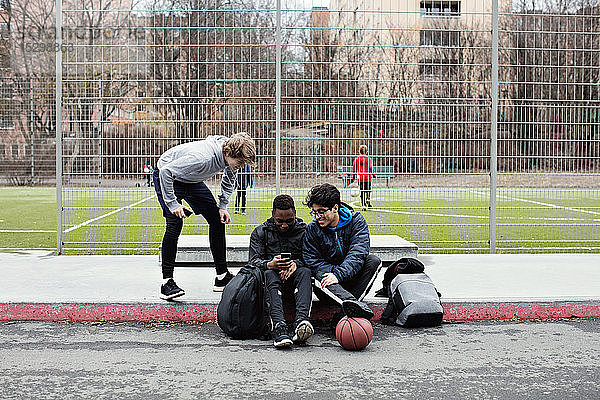 Teenager sieht Freunde an  die soziale Medien auf dem Bürgersteig gegen den Fußballplatz in der Stadt nutzen