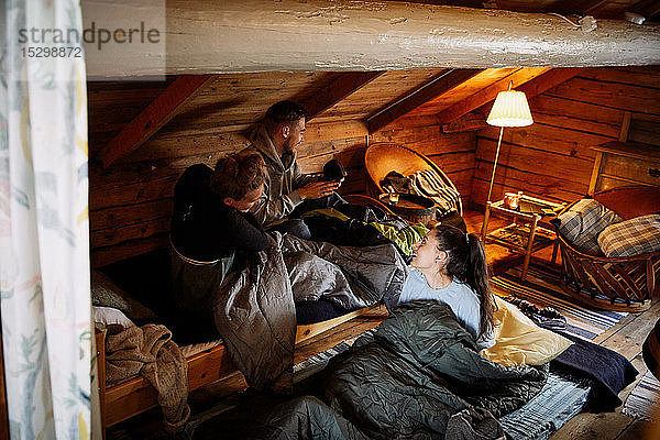 Hochwinkelansicht von Freundinnen und Freunden  die sich unterhalten  während sie zur Schlafenszeit in einer Hütte ruhen