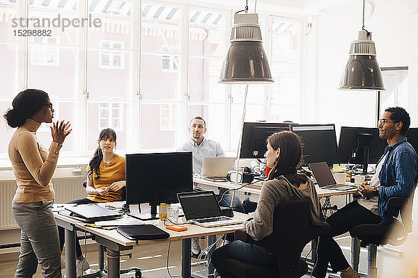 Computerprogrammiererin diskutiert während der Sitzung mit Kollegen am Schreibtisch