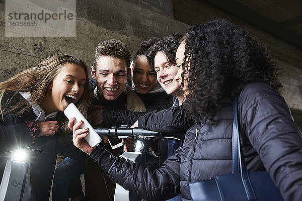 Teenager-Mädchen zeigt glücklichen männlichen und weiblichen Freunden ihr Handy