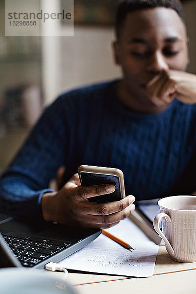 Ernsthafter Teenager benutzt Smartphone beim E-Learning zu Hause