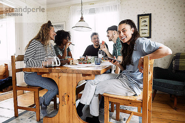 Porträt einer lächelnden jungen Frau  die ein Smartphone benutzt  während sie mit Freunden zu Hause sitzt