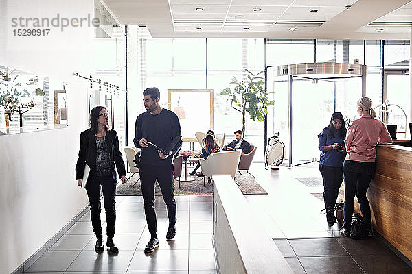 Eine reife Geschäftsfrau diskutiert mit einem männlichen Kollegen  während sie in der Lobby mit Kollegen im Hintergrund arbeitet