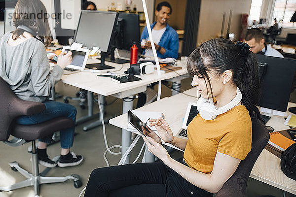Weibliche IT-Computerhackerin nutzt digitales Tablet  während ihre Kollegen im Kreativbüro arbeiten