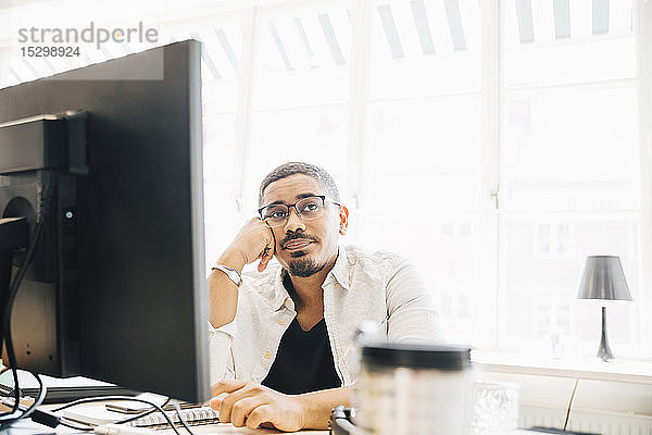 Nachdenklicher Computerprogrammierer schaut weg  während er im Büro am Fenster sitzt