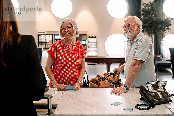 Lächelndes älteres Paar im Gespräch mit der Rezeptionistin im Hotel