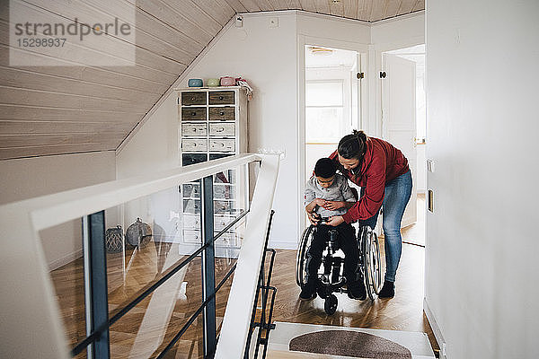 Mutter befestigt Rollstuhl-Schnalle für behinderten Sohn zu Hause