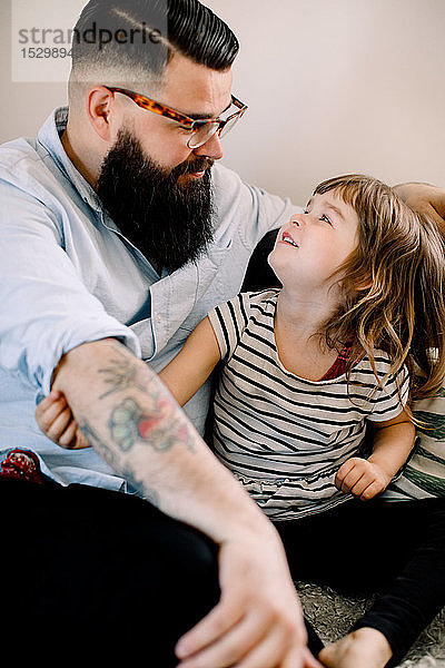 Lächelnder Vater spricht mit Tochter  während er zu Hause auf dem Sofa sitzt
