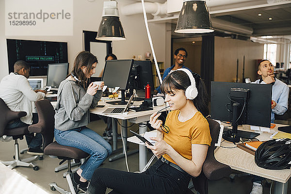 IT-Fachfrau verwendet digitales Tablet  während ihre Kolleginnen im Hintergrund im Kreativbüro arbeiten