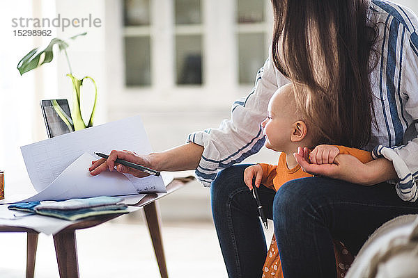 Mittelteil einer berufstätigen Mutter  die Dokumente mit einem kleinen Mädchen im Heimbüro prüft