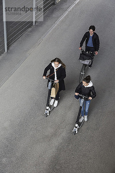 Hochwinkelaufnahme von Freundinnen und Freunden  die auf Elektrorollern und Fahrrädern auf der Straße in der Stadt fahren