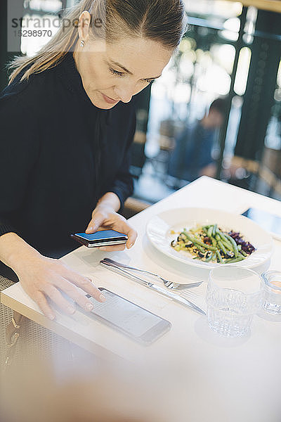 Selbstbewusste Unternehmerin benutzt Mobiltelefon  während sie mit Kreditkarte in der Cafeteria im Büro sitzt