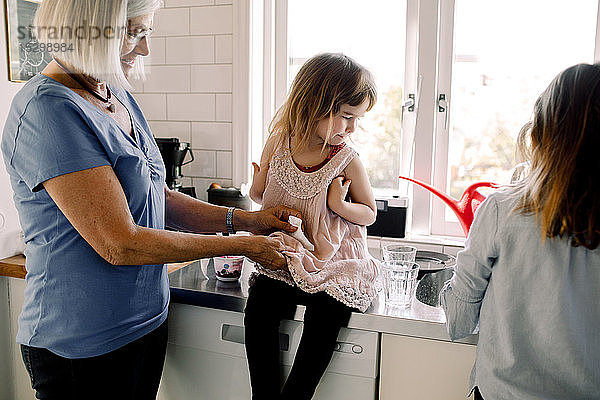 Großmutter reinigt das Kleid einer Enkelin durch ein Mädchen  das in der Küche am Tresen arbeitet