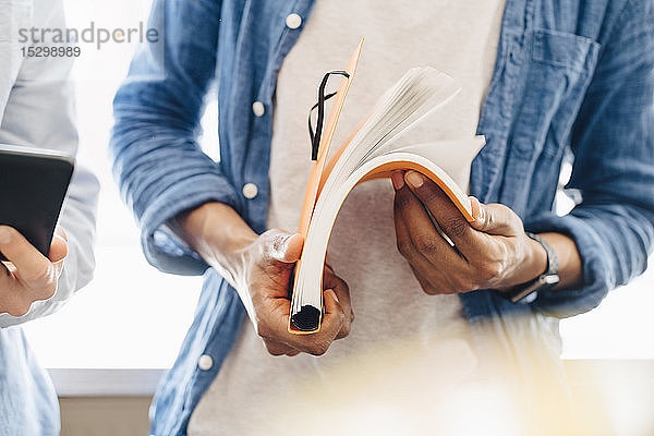 Mittelsektion von Computerprogrammierern mit Buch und digitalem Tablett im Büro stehend