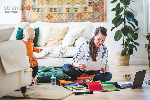 Modedesignerin prüft Papiere  während die Tochter im Wohnzimmer spielt