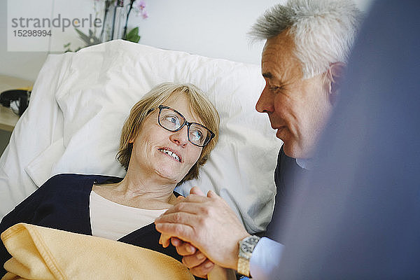 Lächelnde Frau schaut den Seniorpartner an  während sie auf der Krankenhausstation im Bett liegt