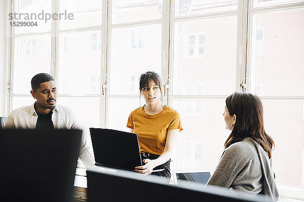 Weibliche Software-Ingenieurin erklärt ihren Kollegen  während sie im Büro am Fenster sitzt