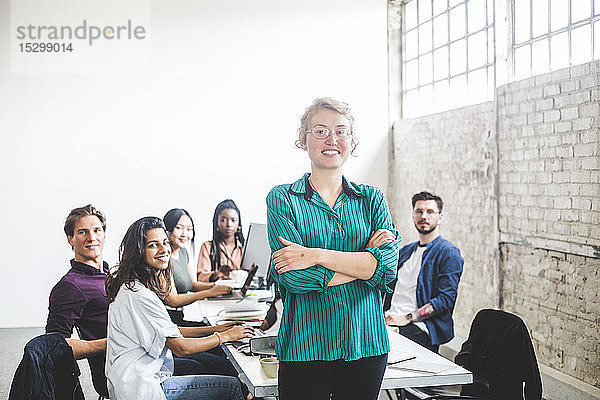 Porträt einer selbstbewusst lächelnden Programmiererin mit Kollegen  die im Sitzungssaal arbeiten