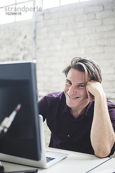 Porträt eines lächelnden jungen männlichen Programmierers  der am Schreibtisch im Büro kodiert