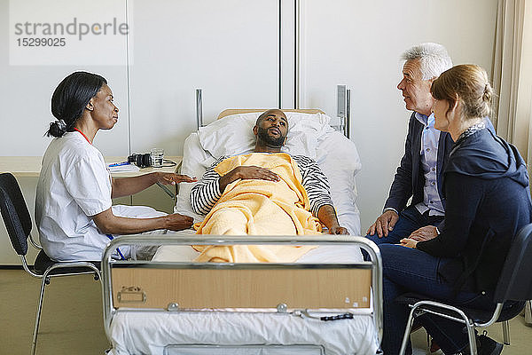 Junger Mann sieht Familie an  während der Arzt auf der Krankenhausstation diskutiert
