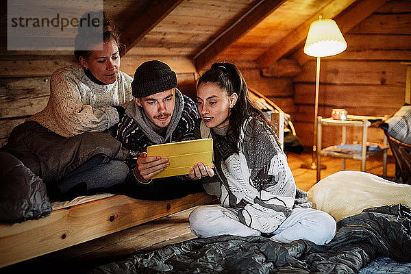Freunde schauen einen Film über ein digitales Tablet an  während sie sich in einem Ferienhaus entspannen