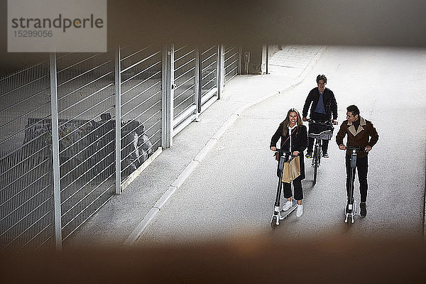 Hochwinkelaufnahme von männlichen und weiblichen Teenager-Freunden  die auf Elektrorollern und Fahrrädern auf der Straße in der Stadt fahren