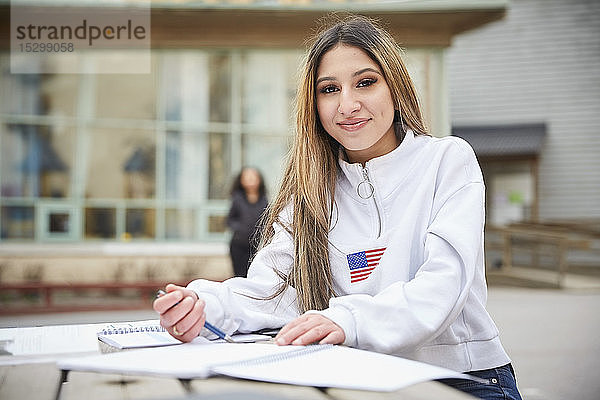 Porträt eines selbstbewussten Teenagers  der am Tisch auf dem Schulhof sitzt