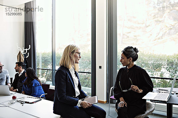Geschäftsfrauen diskutieren im Sitzungssaal mit Kollegen  die im Hintergrund arbeiten