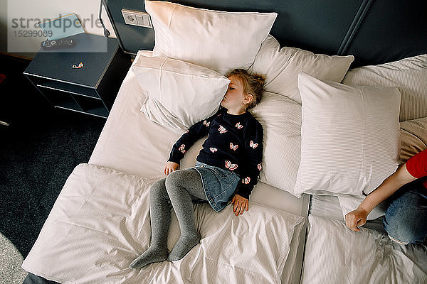 Hochwinkelansicht eines auf dem Bett im Hotelzimmer liegenden Mädchens