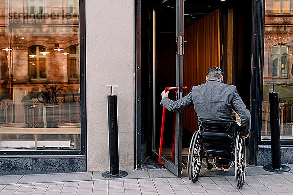 Rückansicht eines behinderten reifen Mannes  der beim Betreten des Ladens auf einem Rollstuhl sitzt