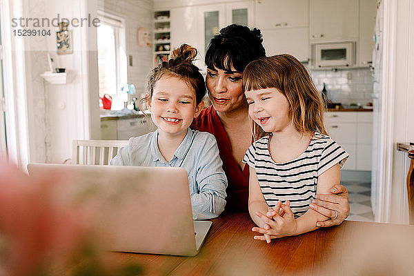 Mutter und Töchter schauen auf den Laptop  während sie im Wohnzimmer sitzen