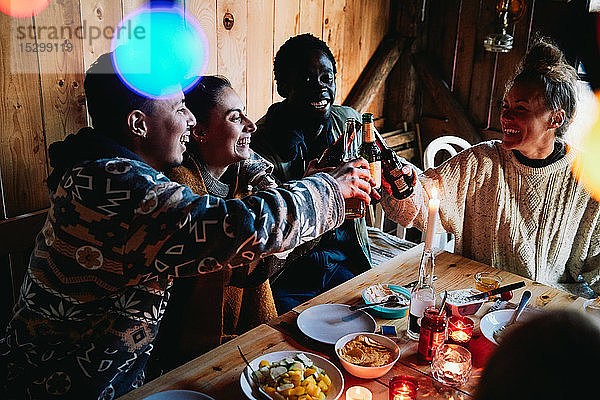 Hochwinkelaufnahme eines glücklichen Mannes und seiner Freunde  die in einer Blockhütte auf Bierflaschen anstoßen