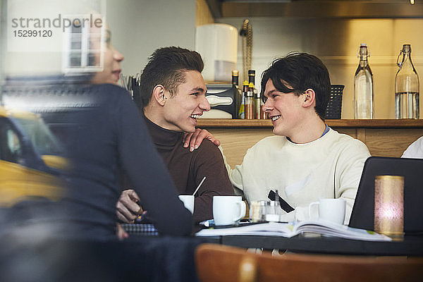 Lächelnde männliche Freunde im Teenageralter sitzen am Tisch im Restaurant