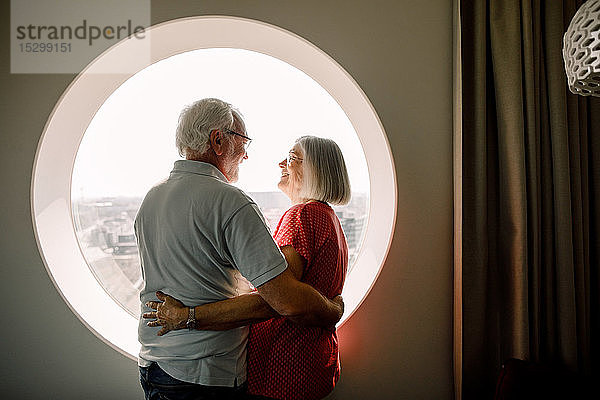 Älteres Paar umarmt sich  während es am Fenster im Hotelzimmer steht