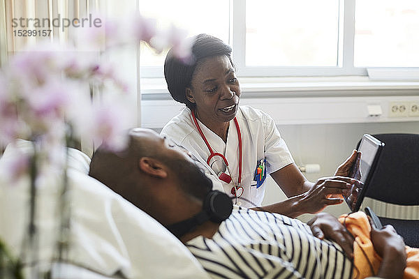 Älterer Arzt zeigt männlichen Patienten digitale Tablette bei Routinebesuch im Krankenhaus