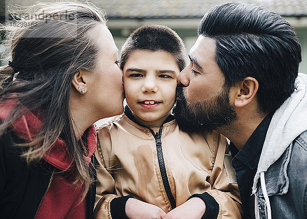 Seitenansicht von Eltern  die ihren autistischen Sohn im Hof küssen
