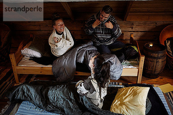 Hochwinkelansicht von lächelnden Freunden  die sich unterhalten  während sie zur Schlafenszeit in der Hütte ruhen