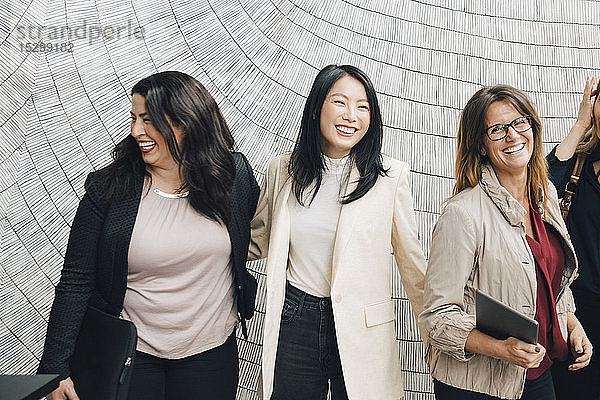 Lächelnde multi-ethnische Geschäftsfrauen stehen im Büro an der Wand