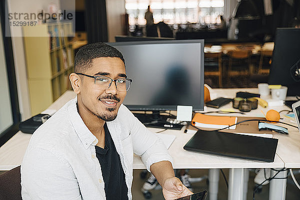 Porträt eines selbstbewussten Computer-Hackers  der im Büro am Schreibtisch sitzt